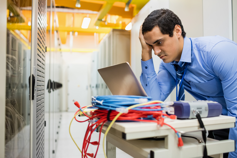 Stressed technician using laptop in server room